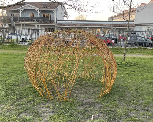 Oeuvre en osier en forme de boule avec un espace pour entrer dessous, dans un parc de la ville de Biganos