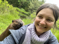 Portrait de Suzanne Husky, en pleine nature. Un castor est derri&egrave;re son &eacute;paule, elle sourit.